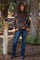 woman wearing a brown floral maternity top and dark jeans, standing outdoors among trees
