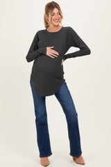 woman wearing a dark gray long sleeve maternity top and blue jeans, gently resting her hands on her baby bump