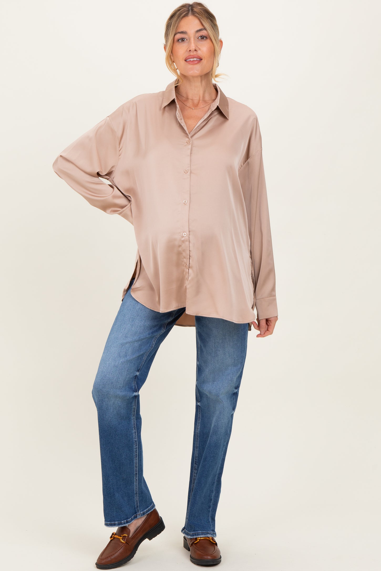 woman wearing a beige long sleeve maternity shirt with a relaxed fit and jeans, holding her baby bump