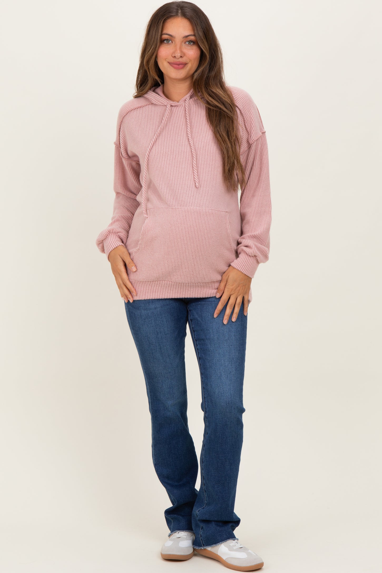 woman wearing a pink ribbed maternity hoodie with a relaxed fit and jeans, showcasing her baby bump