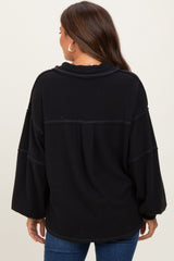 woman wearing a black oversized ribbed maternity top, showing a relaxed fit and long sleeves from the back