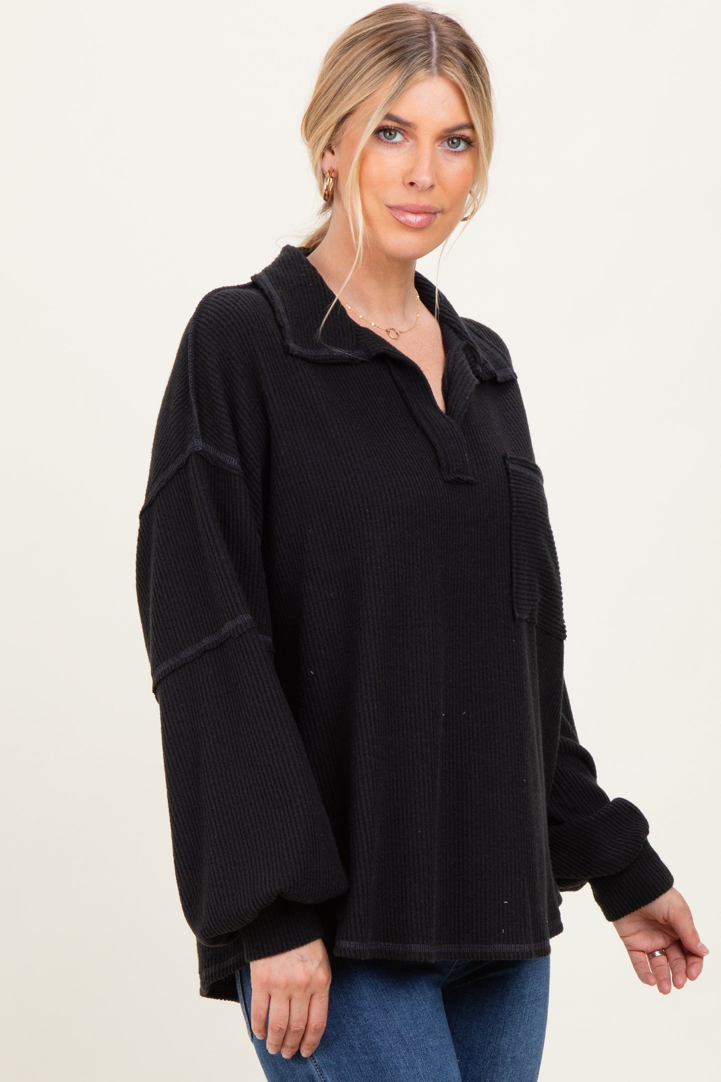 woman wearing a black oversized waffle knit pullover with a collar and front pocket, styled with blue jeans