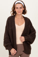 woman wearing a dark brown chunky knit cardigan over a beige top with ribbed sleeves and a relaxed fit