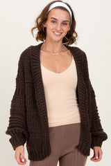 woman wearing a dark brown chunky knit cardigan over a beige v-neck top and ribbed pants