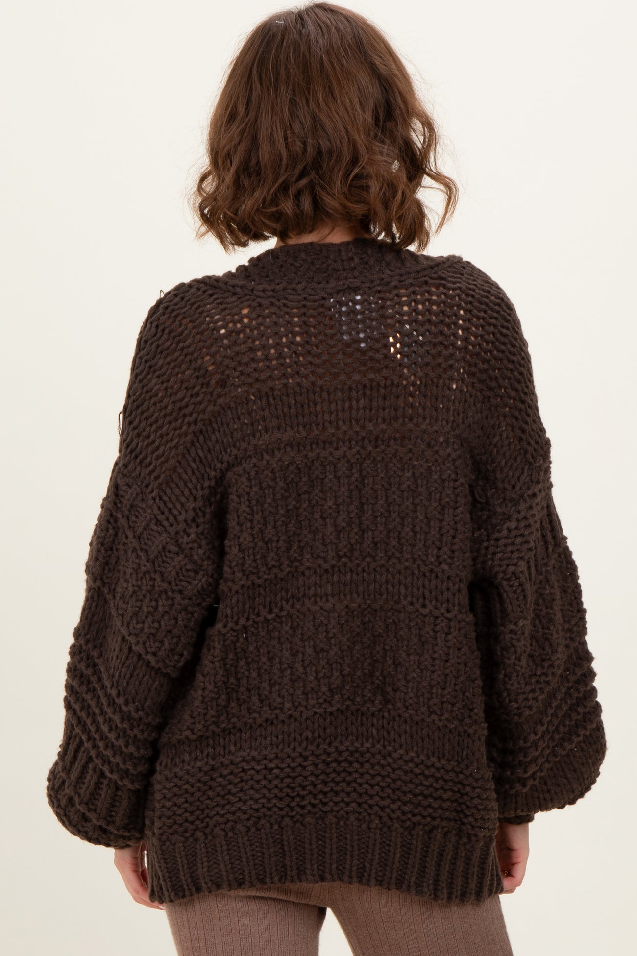 woman wearing a chunky dark brown knit sweater with oversized sleeves, viewed from the back
