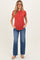woman wearing a rust short sleeve maternity top and blue flared jeans, holding her baby bump