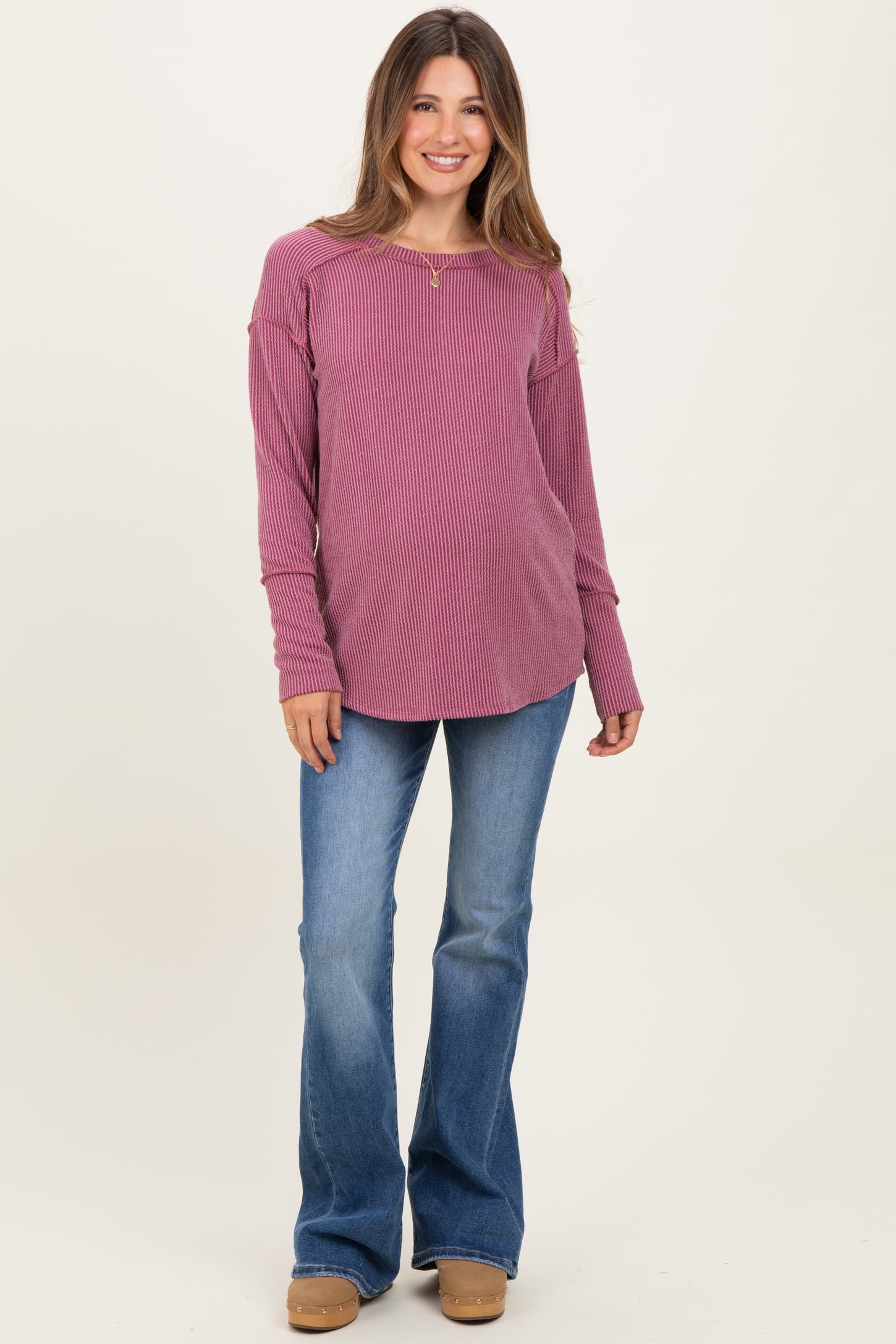 woman wearing a mauve ribbed long sleeve maternity top and blue flared jeans, showing a casual and stylish look