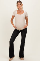 woman wearing a beige short sleeve maternity top with a scoop neck and bow detail, paired with black flared maternity pants and showing her baby bump