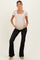 woman wearing a beige short sleeve maternity top with a scoop neck and bow detail, paired with black flared maternity pants and showing her baby bump