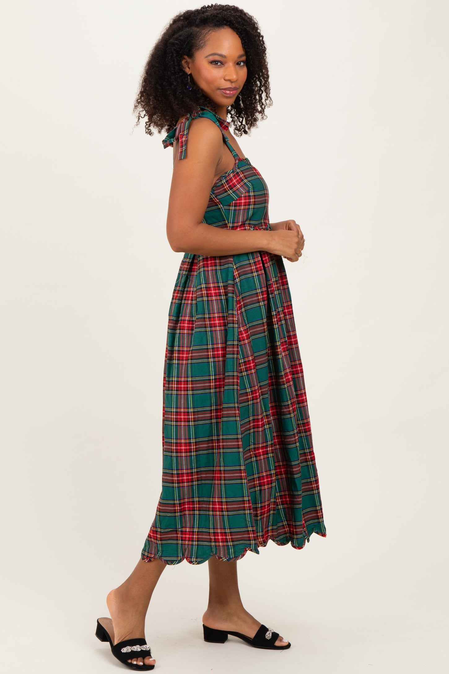 woman wearing a green plaid midi dress with tie shoulder straps and a scalloped hem