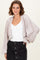 woman wearing a light pink oversized cardigan with bell sleeves over a white top and a black denim skirt