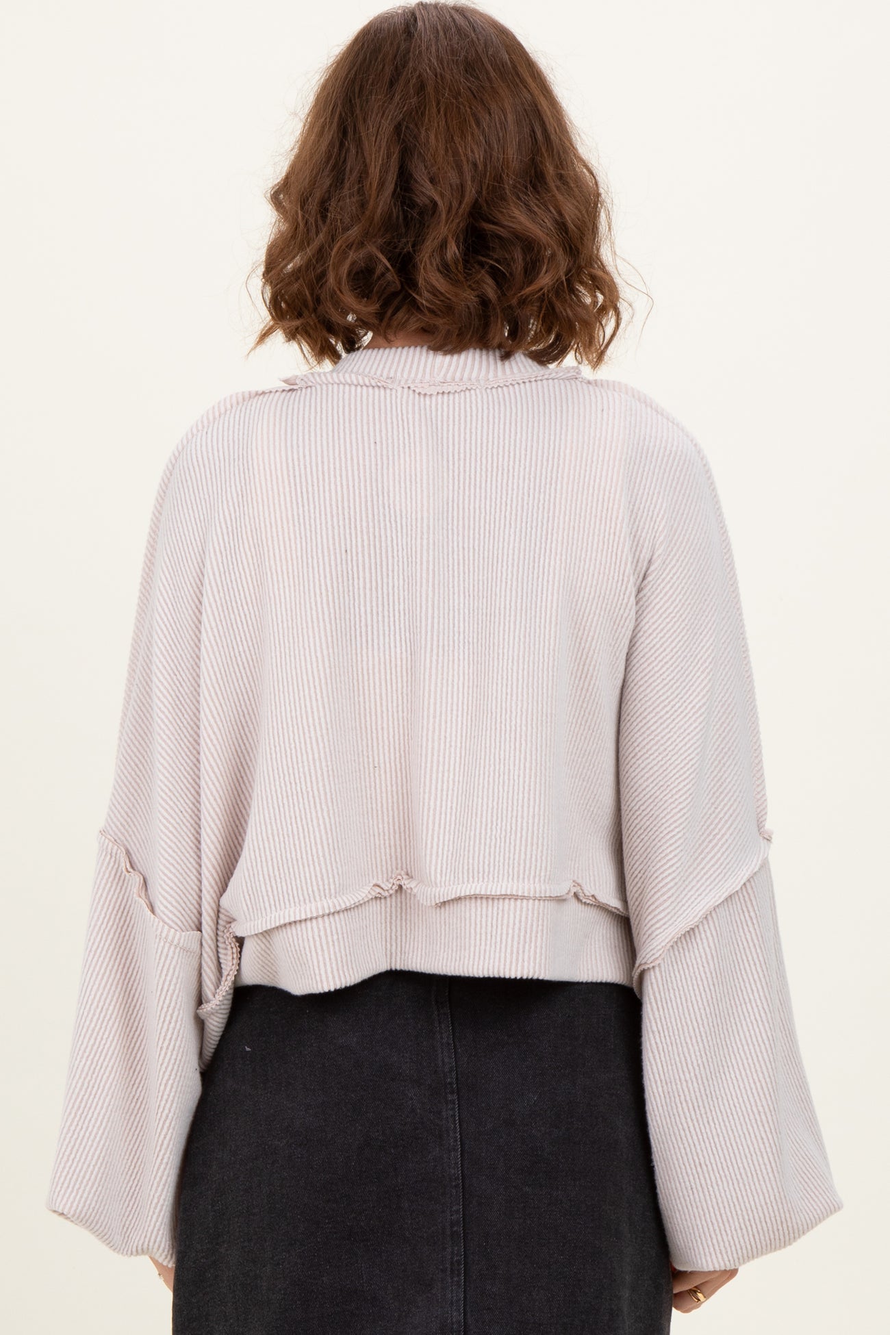 woman wearing a light pink cropped ribbed sweater with bell sleeves, viewed from the back