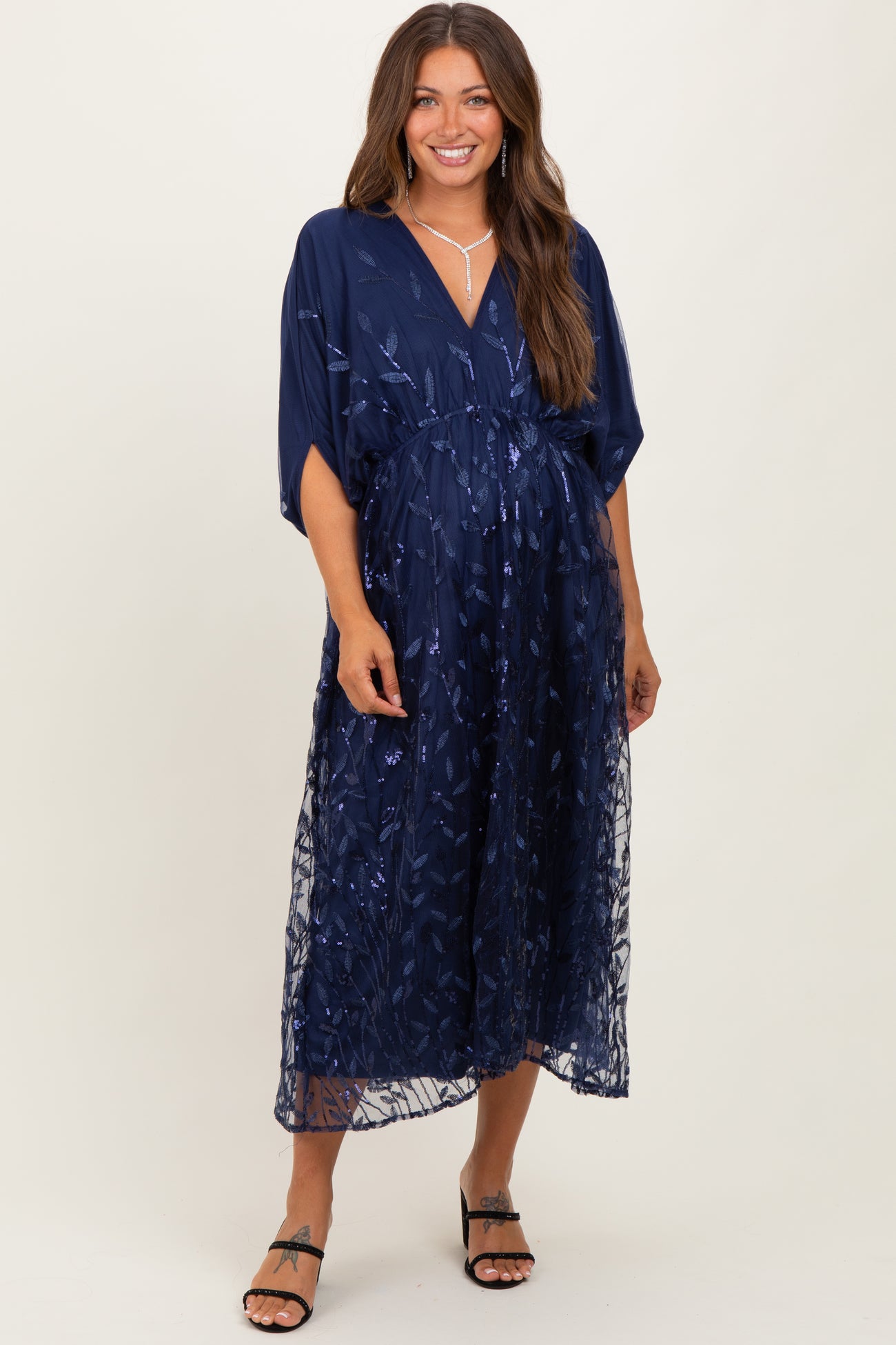 woman wearing a navy blue maternity dress with floral embroidery and a flowing skirt, showcasing her baby bump