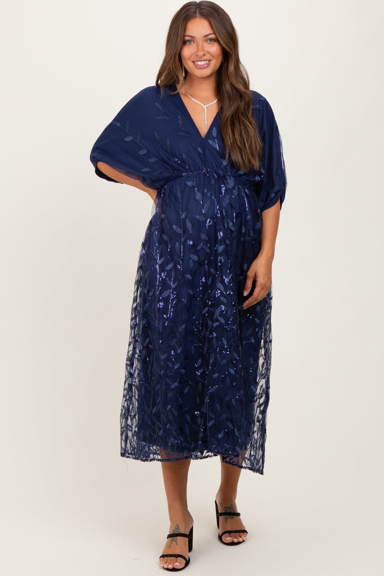 woman wearing a navy blue maternity dress with floral embroidery and a wrap style, showcasing her baby bump