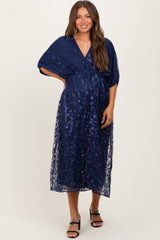 woman wearing a navy blue maternity dress with floral embroidery and a wrap style, showcasing her baby bump