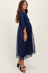 woman wearing a navy blue maternity dress with sheer overlay and embroidered details, showing her baby bump