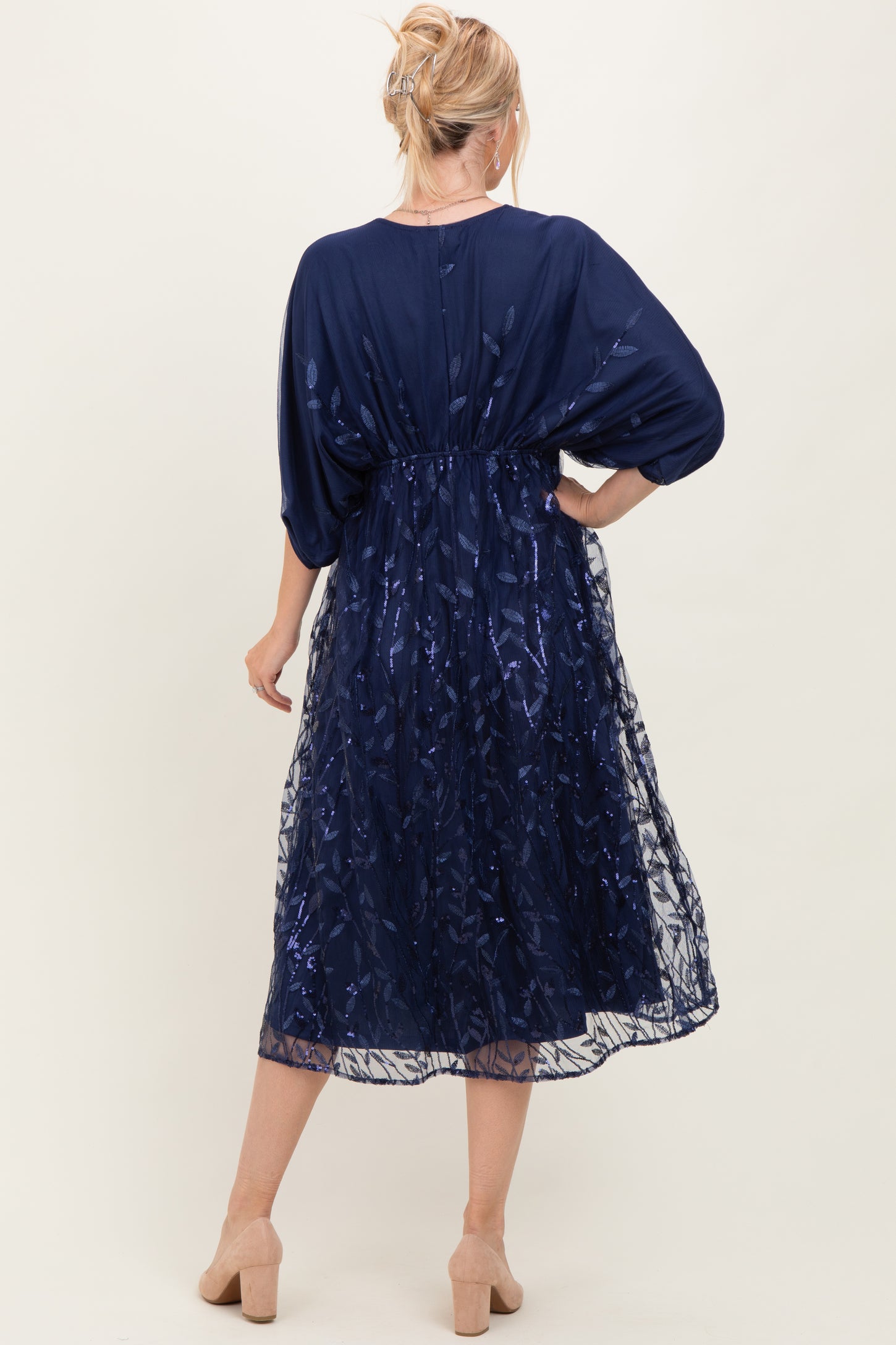 woman wearing a navy blue dress with sheer overlay and flutter sleeves, styled with a fitted waist and mid-calf length