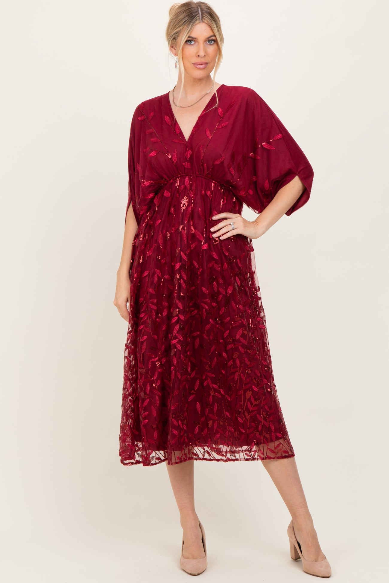 woman wearing a deep red embroidered midi dress with short sleeves and a wrap silhouette, styled with nude heels