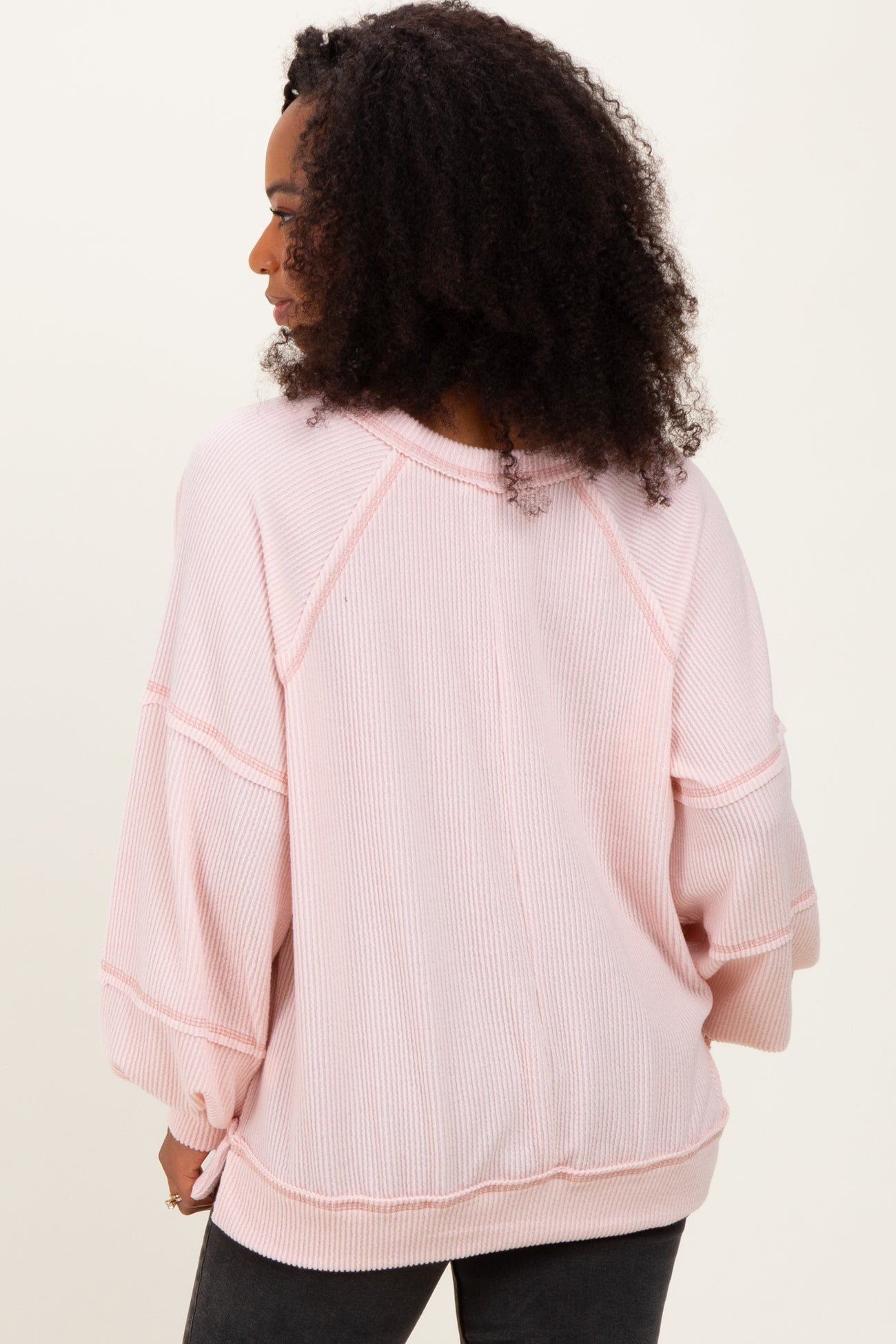 woman wearing a light pink oversized ribbed sweater with three-quarter sleeves and a relaxed fit.