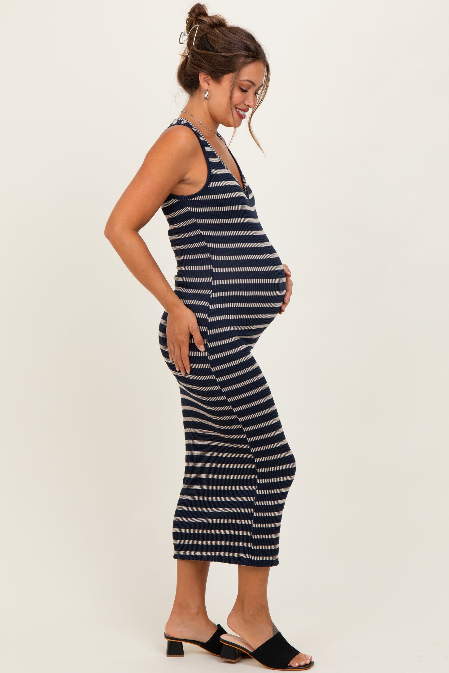 woman wearing a navy and white striped maternity midi dress, gently holding her baby bump while smiling