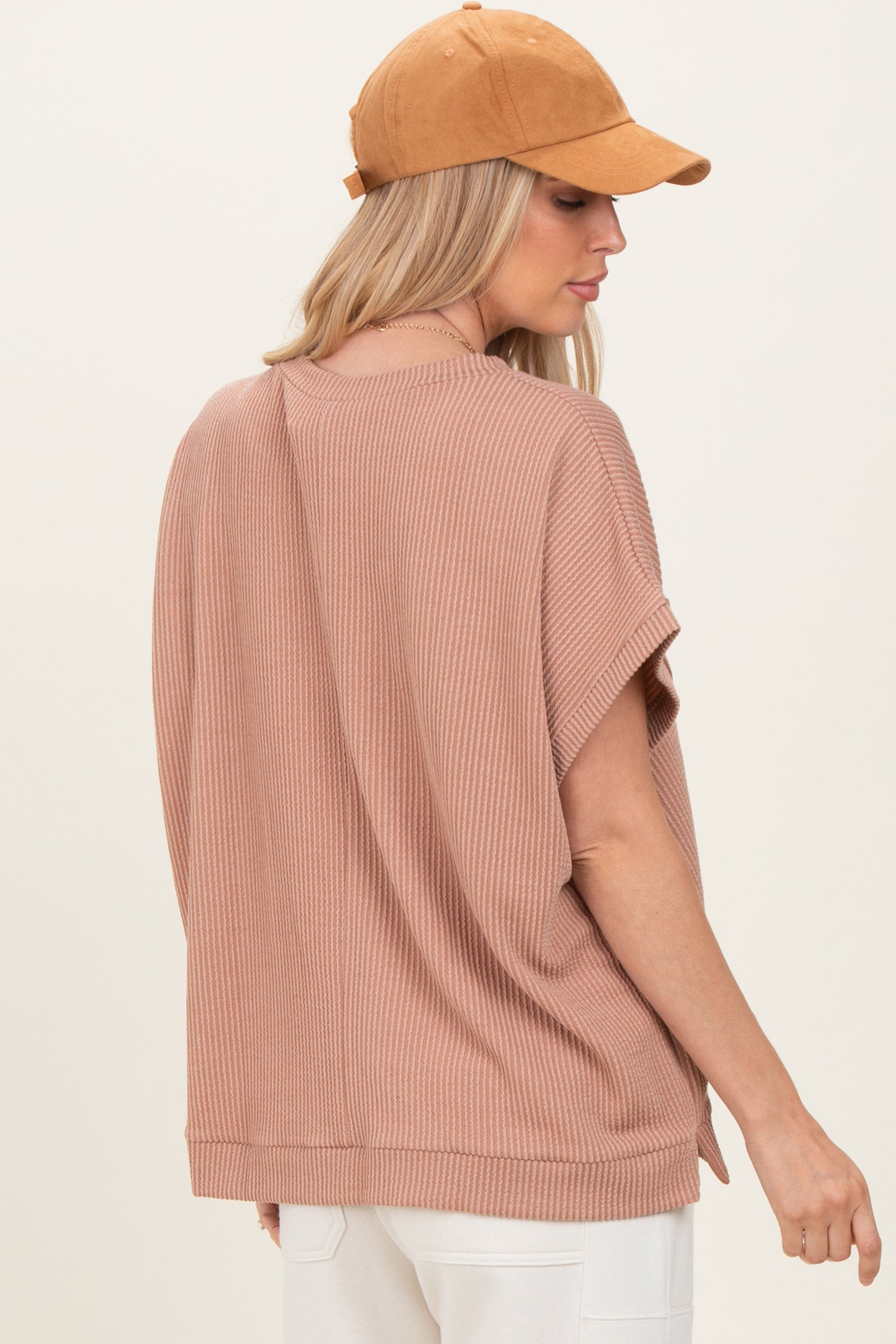 woman wearing a dusty rose oversized ribbed top with short sleeves, styled with a tan baseball cap
