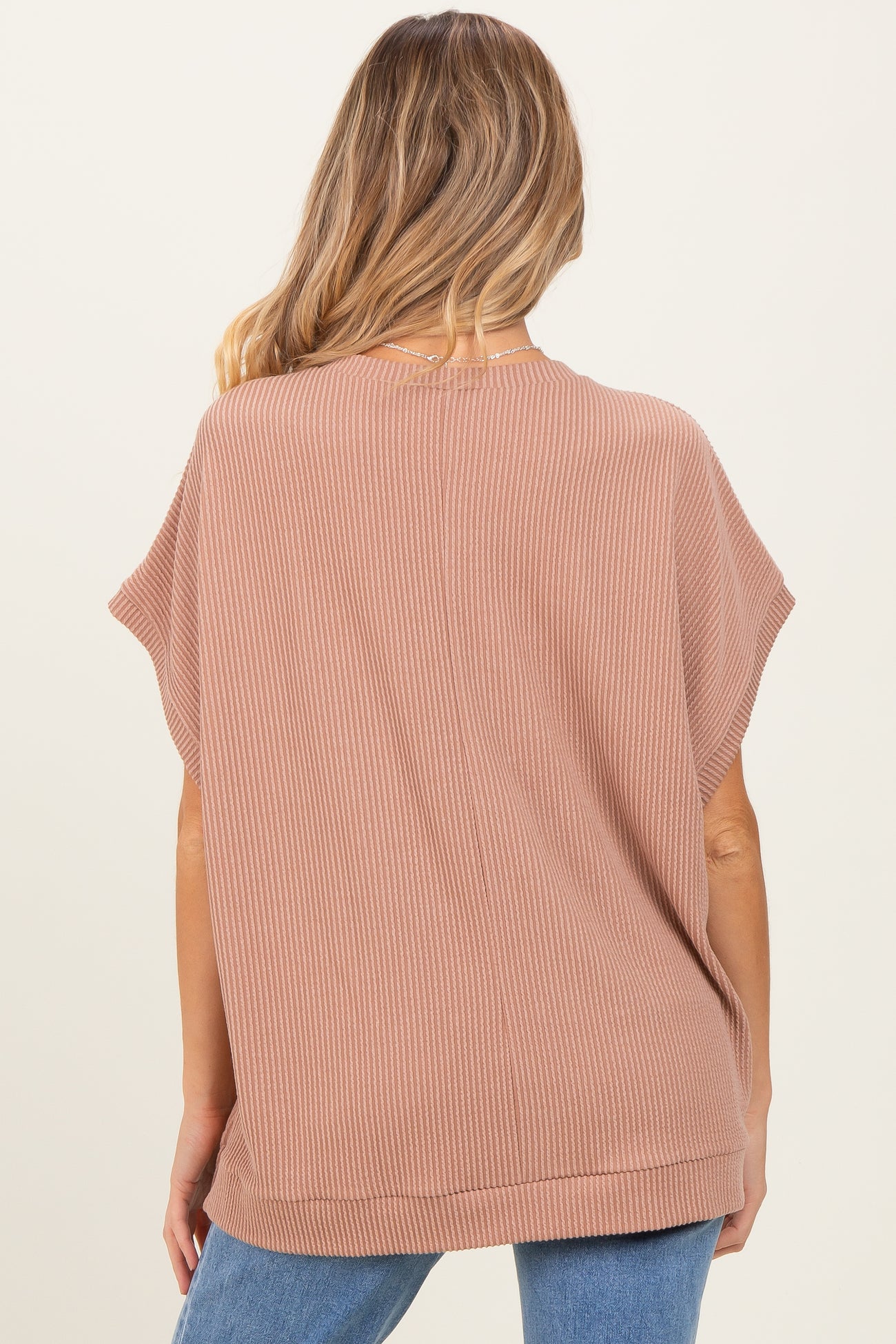woman wearing a loose-fitting ribbed maternity top in pink, showing the back view