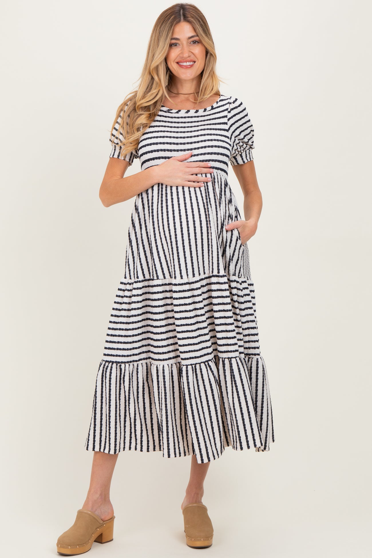 woman wearing a striped maternity maxi dress with puff sleeves and pockets, holding her baby bump