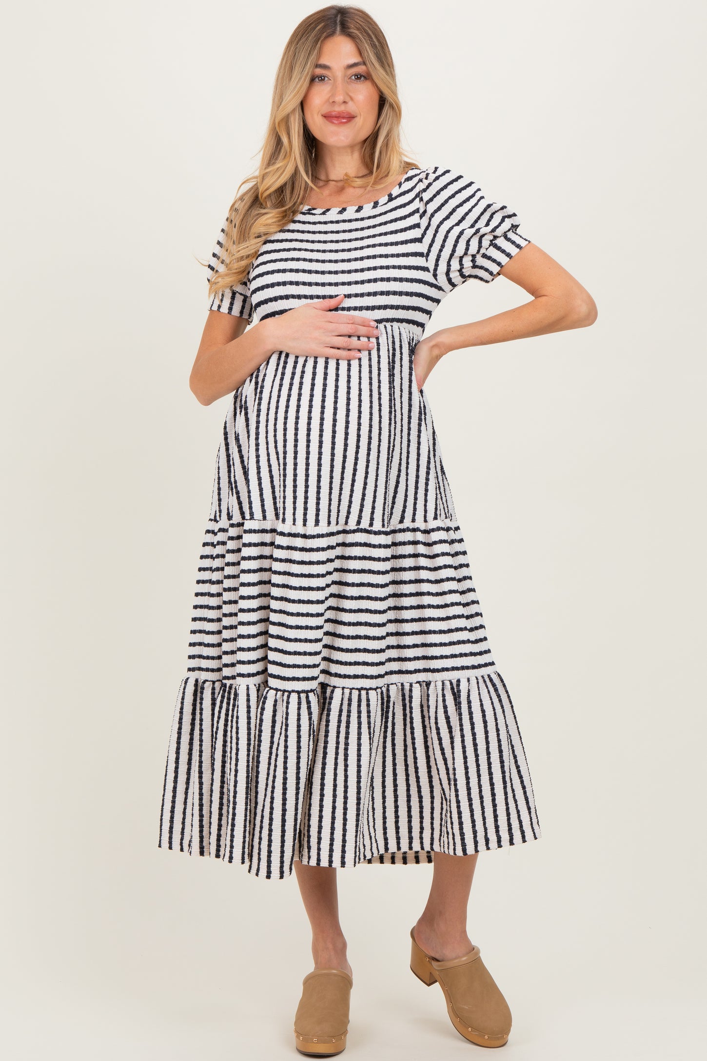 woman wearing a striped maternity dress with tiered skirt and short sleeves, holding her baby bump