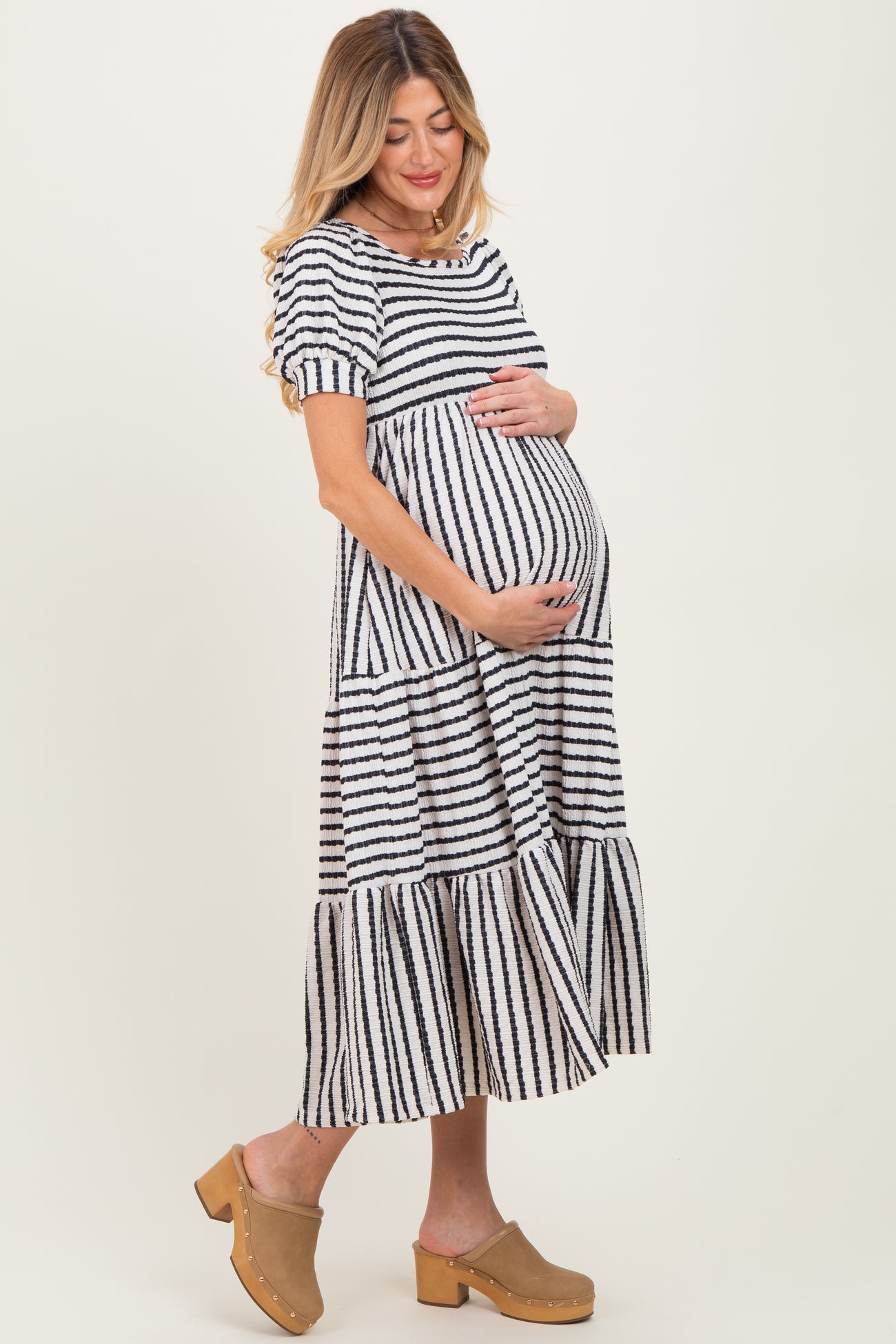 woman wearing a black and white striped maternity dress with short sleeves and a tiered skirt, holding her baby bump