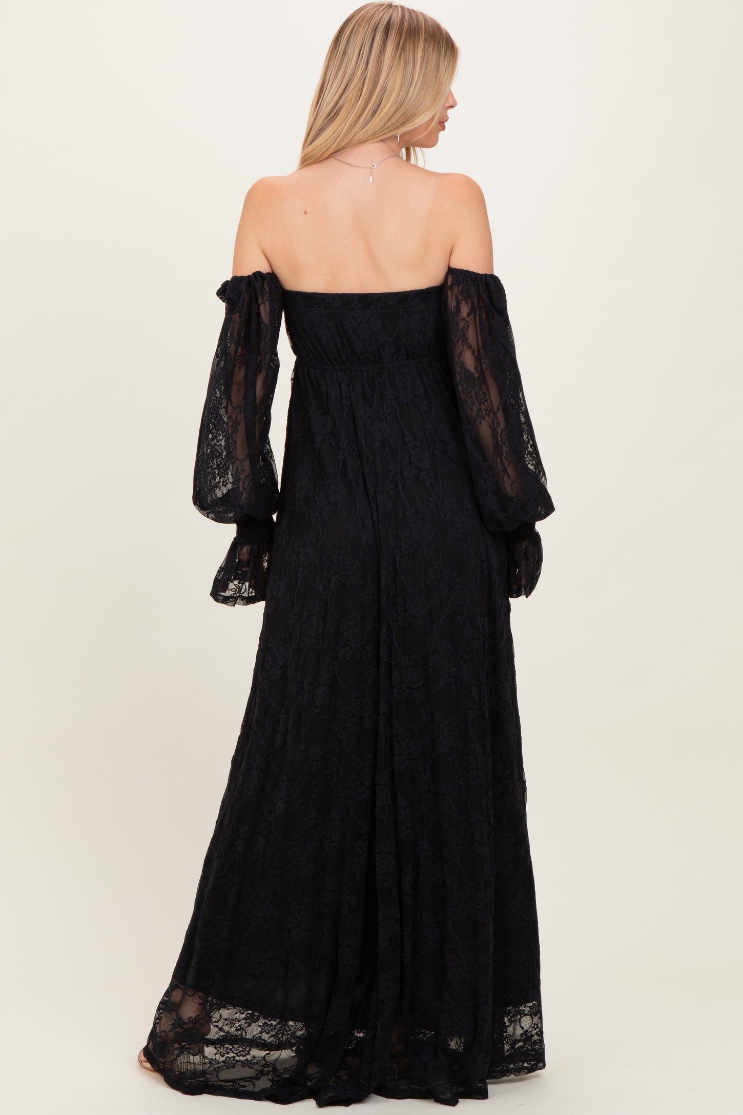 woman wearing a black off-shoulder lace maxi dress with long, puffed sleeves, shown from the back