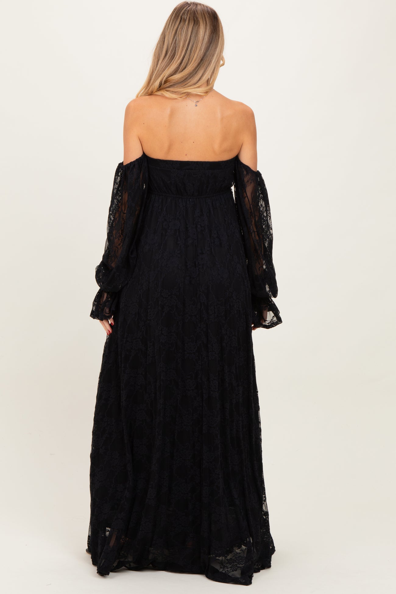 woman wearing a black off-the-shoulder lace maternity dress with long sleeves, showing a flowing silhouette from the back