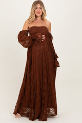 woman wearing a brown lace off-the-shoulder maxi maternity dress, cradling her baby bump