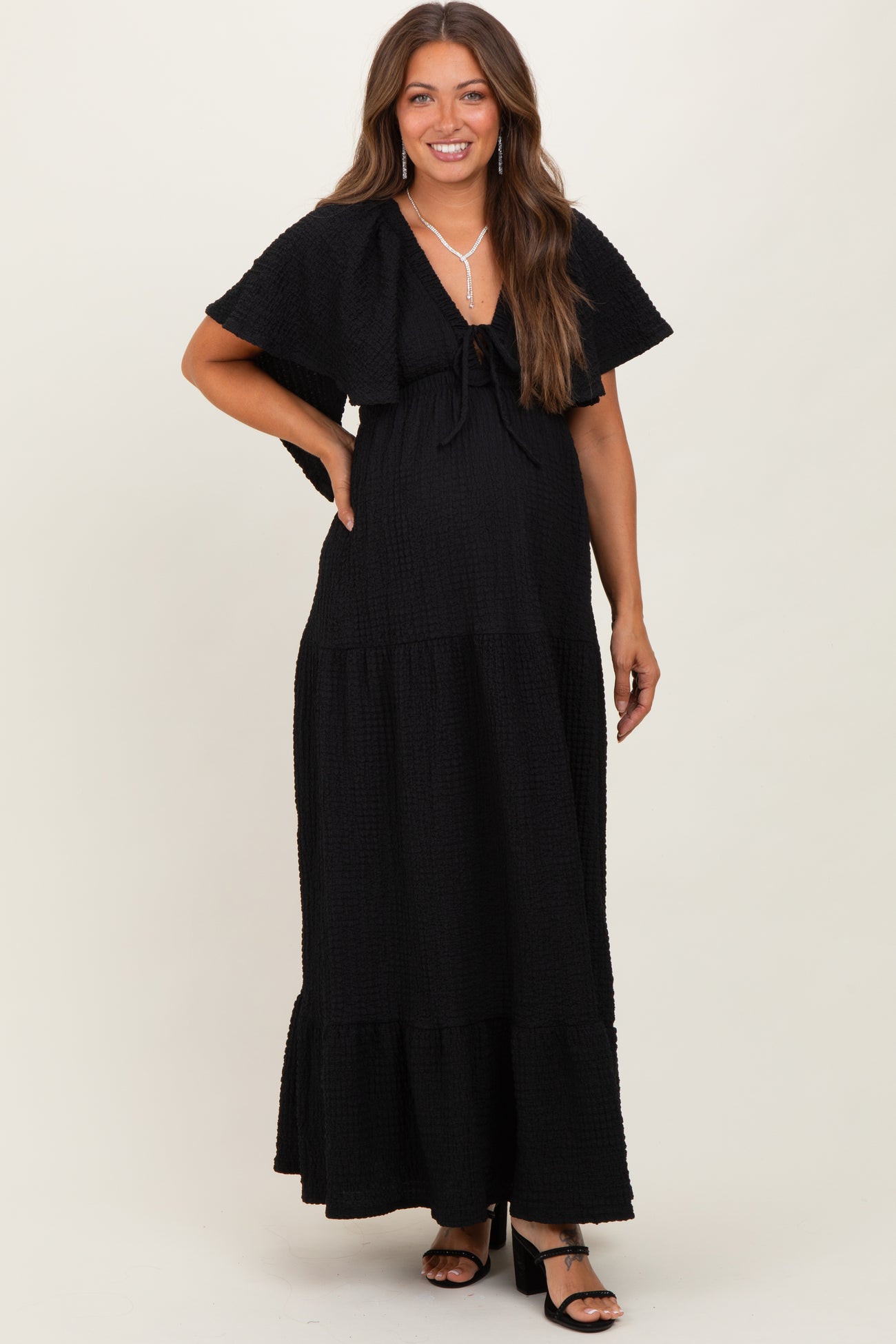 woman wearing a black maternity maxi dress with a tie front and tiered skirt, showcasing her baby bump