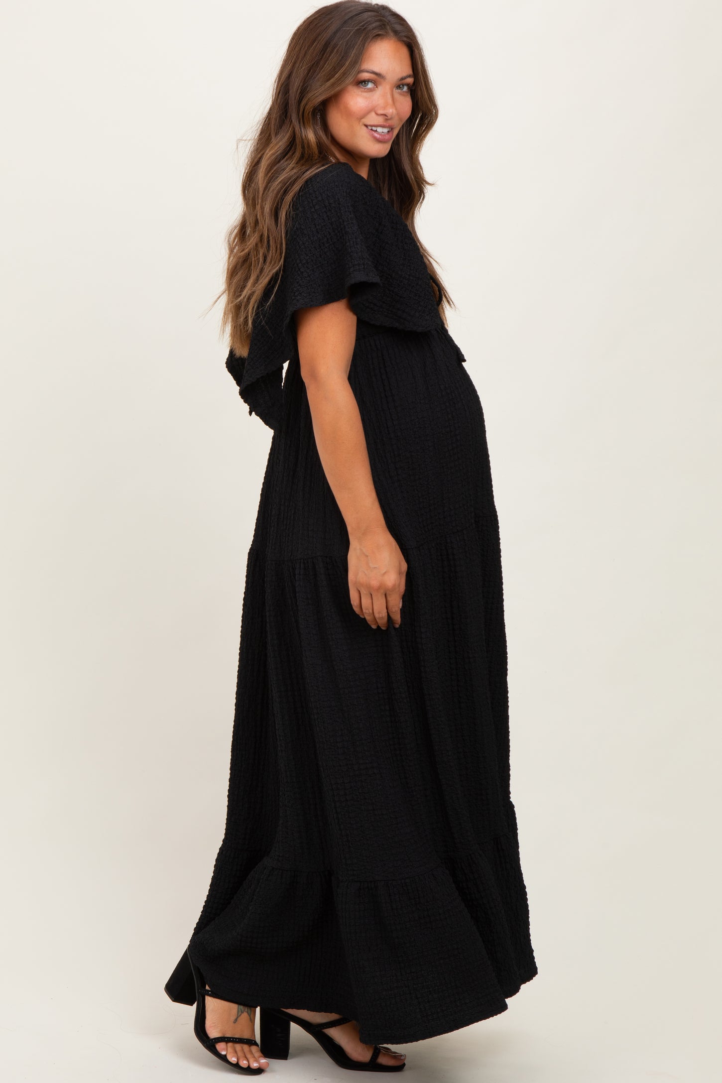 woman wearing a black maternity maxi dress with tiered ruffles and a visible baby bump