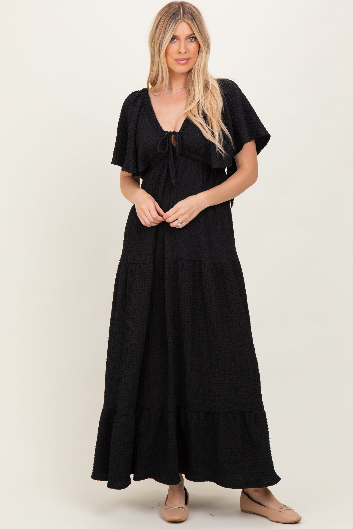 woman wearing a black tiered maxi dress with short sleeves and a tie front detail