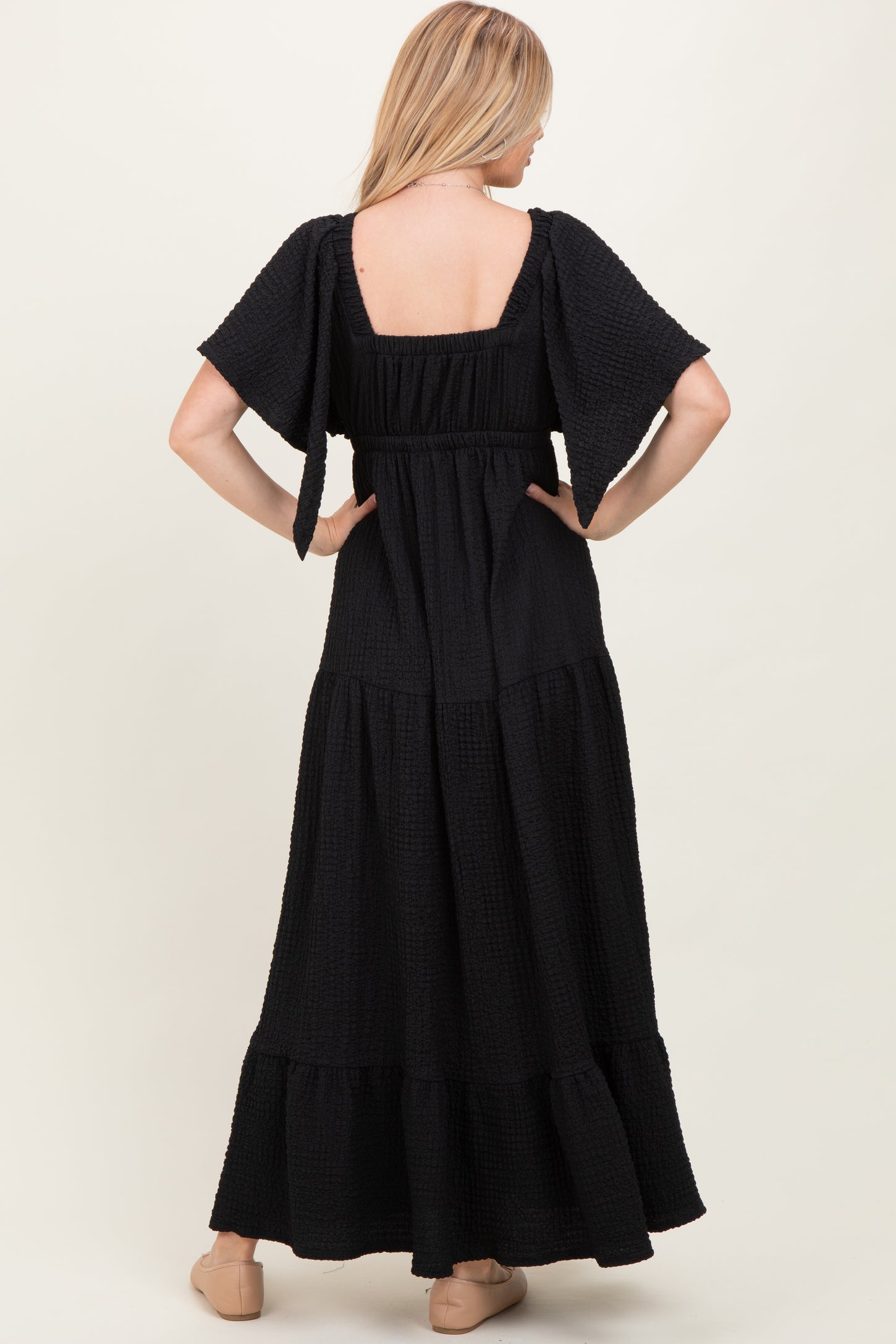 woman wearing a black maxi dress with short flutter sleeves and a tiered skirt, showing the back view
