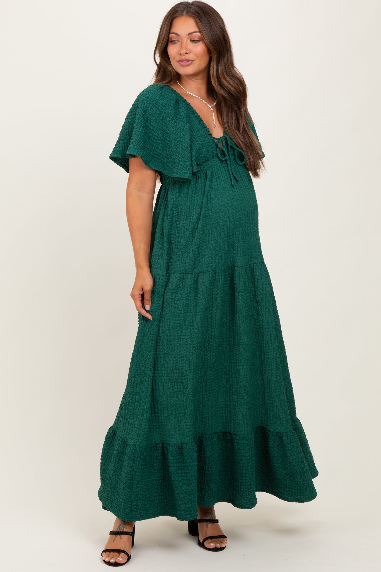 woman wearing a green flutter sleeve maternity maxi dress with a tie front and tiered hemline