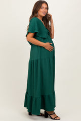 woman wearing a dark green maternity maxi dress with tiered ruffles and a tie front, gently cradling her baby bump