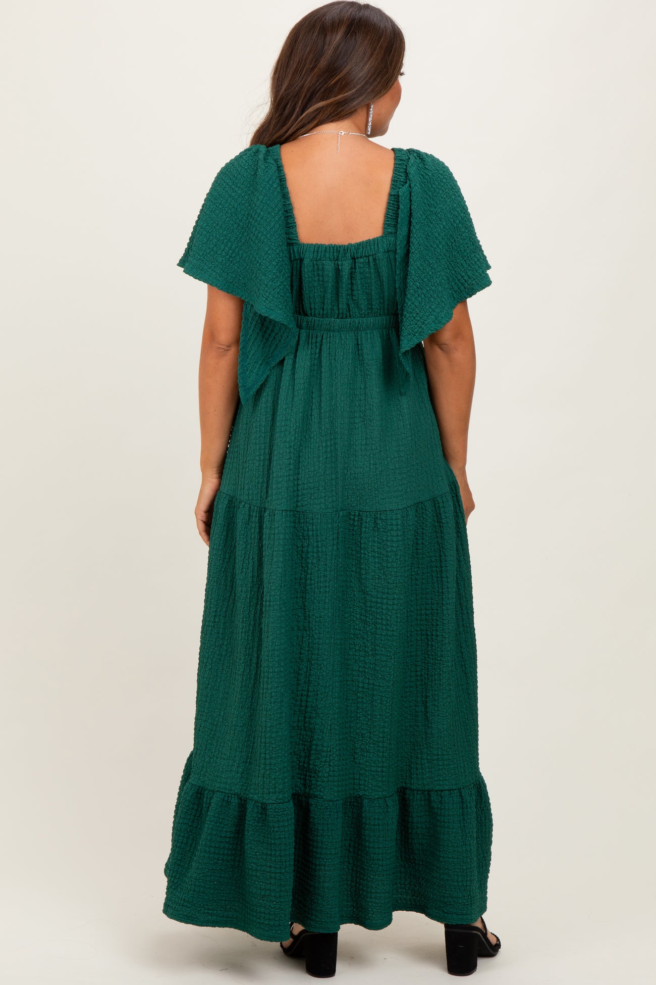 woman wearing a green tiered maternity maxi dress with flutter sleeves, showing the back view