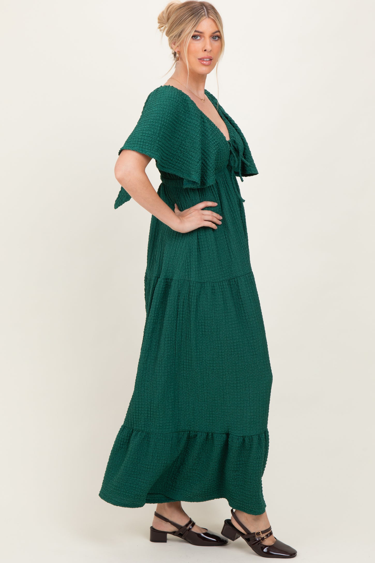woman wearing a dark green tiered maxi dress with flutter sleeves and a tie front detail