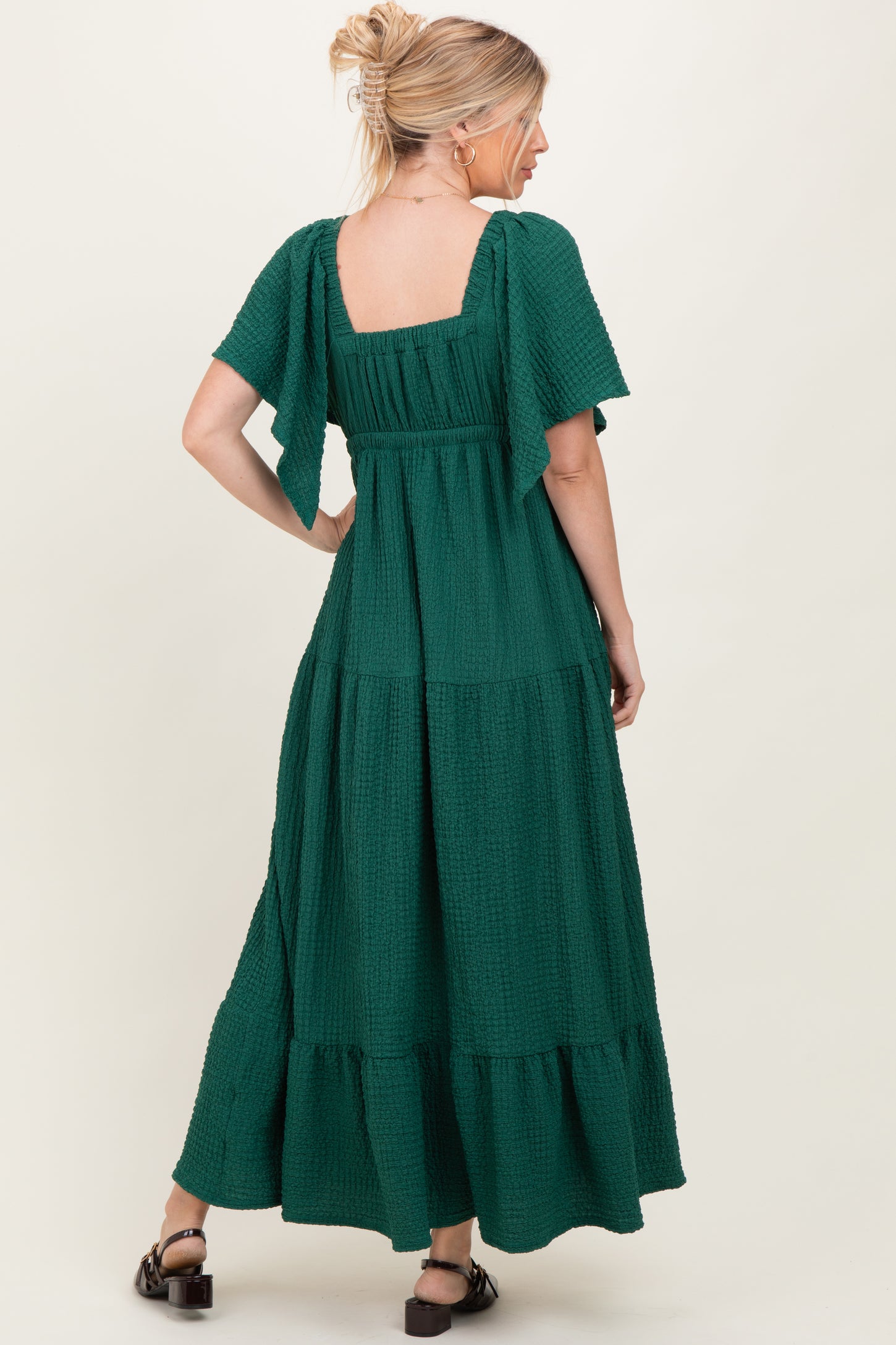 woman wearing a green maxi dress with short flutter sleeves and a tiered design, seen from the back