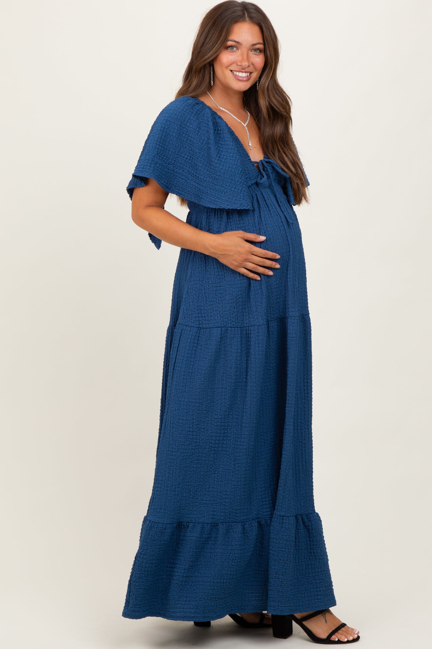 woman wearing a navy blue maternity maxi dress with tiered ruffles and tie detail, showing her baby bump