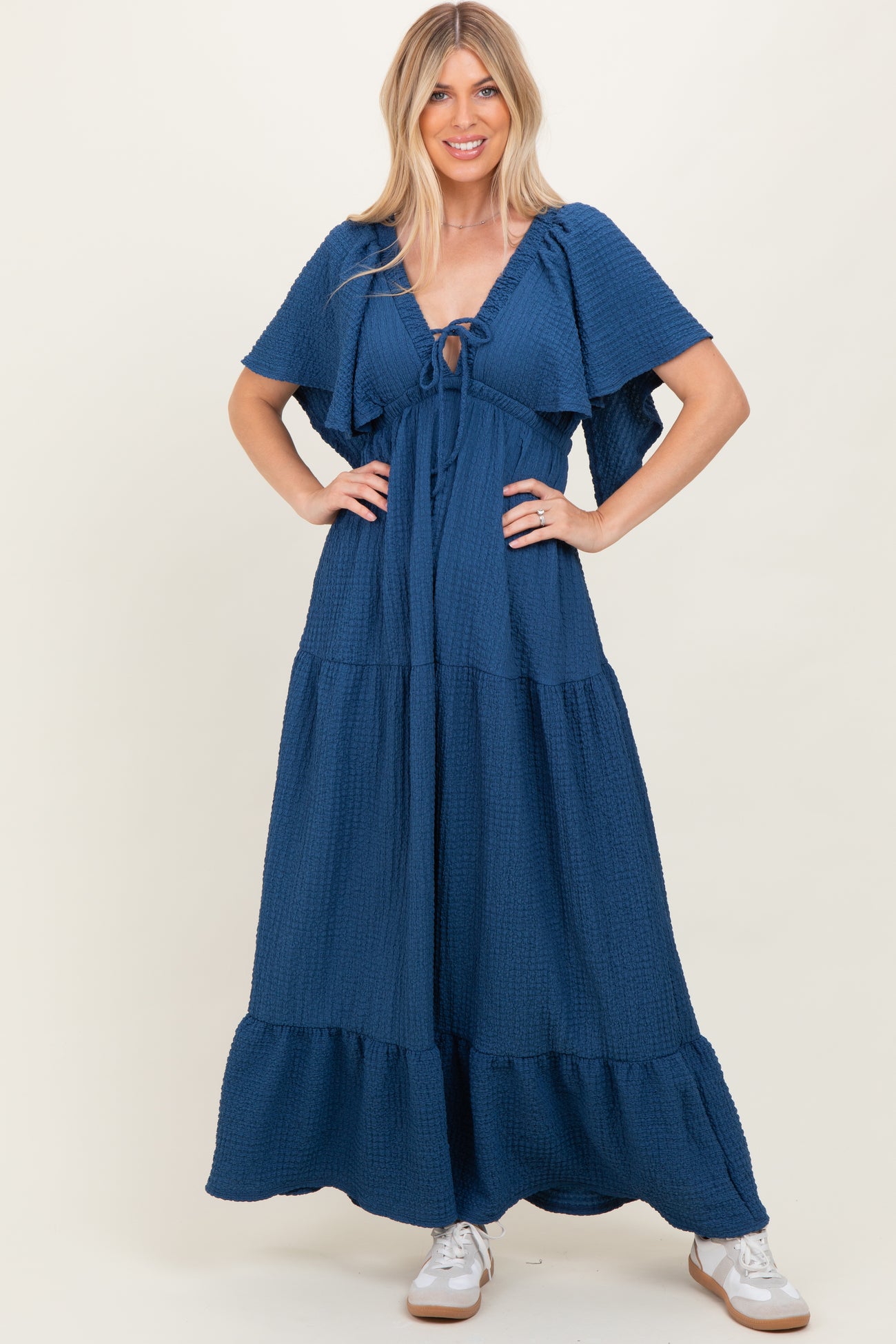 woman wearing a navy blue tiered maxi dress with flutter sleeves and a front tie detail