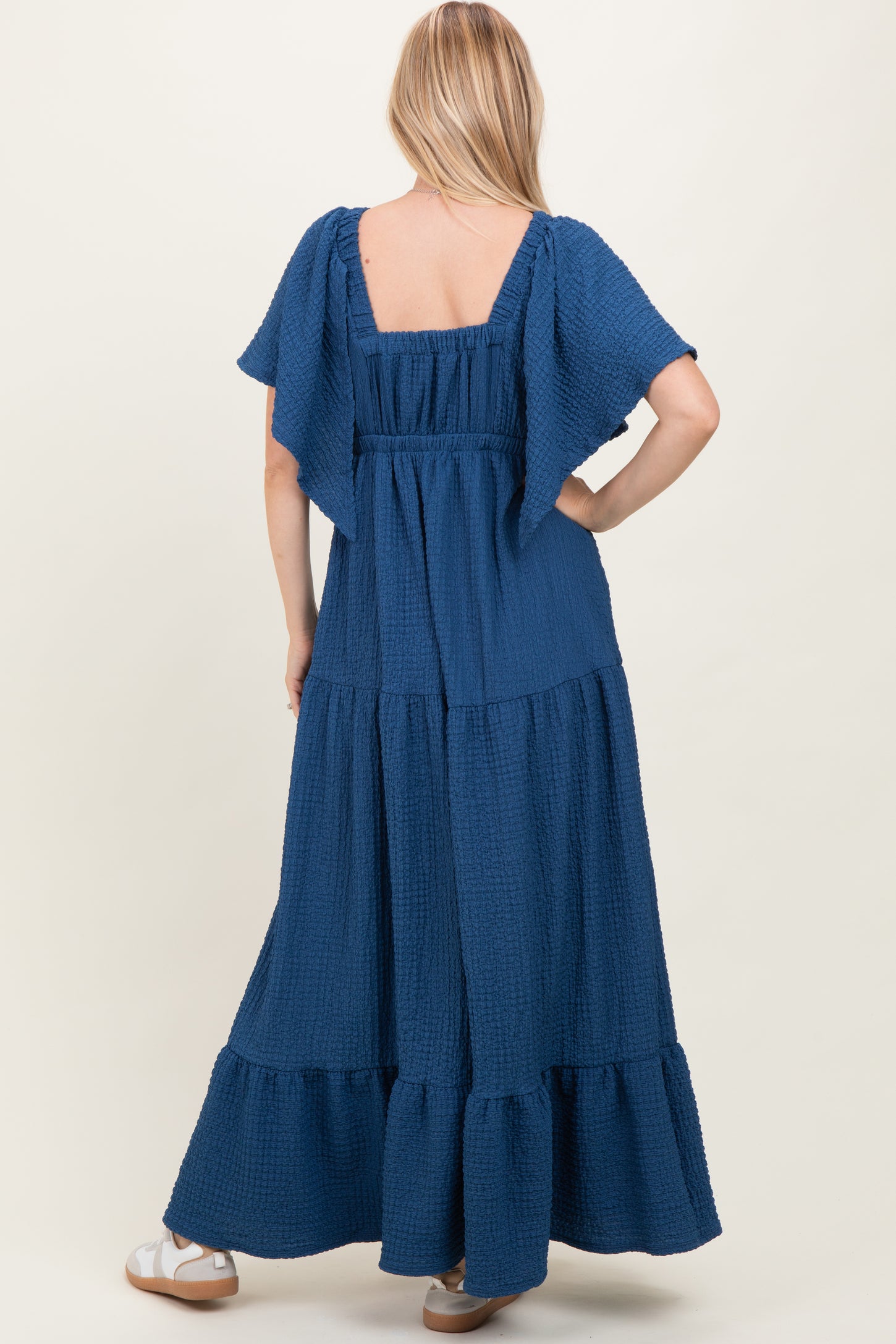 woman wearing a navy blue maxi dress with flutter sleeves and a tiered skirt, shown from the back