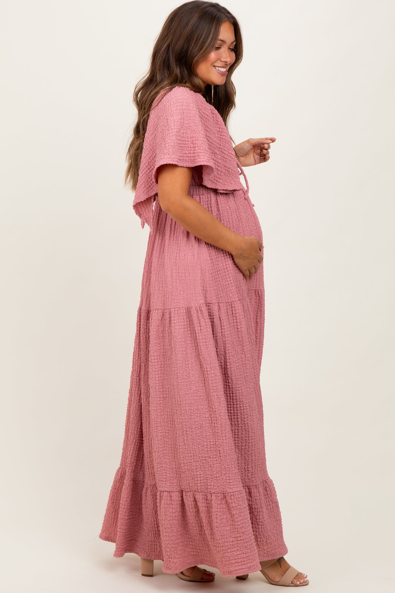woman wearing a pink maternity maxi dress with flutter sleeves and pockets, showing her baby bump