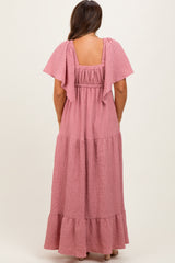 woman wearing a light pink maternity maxi dress with flutter sleeves and a tiered skirt from the back