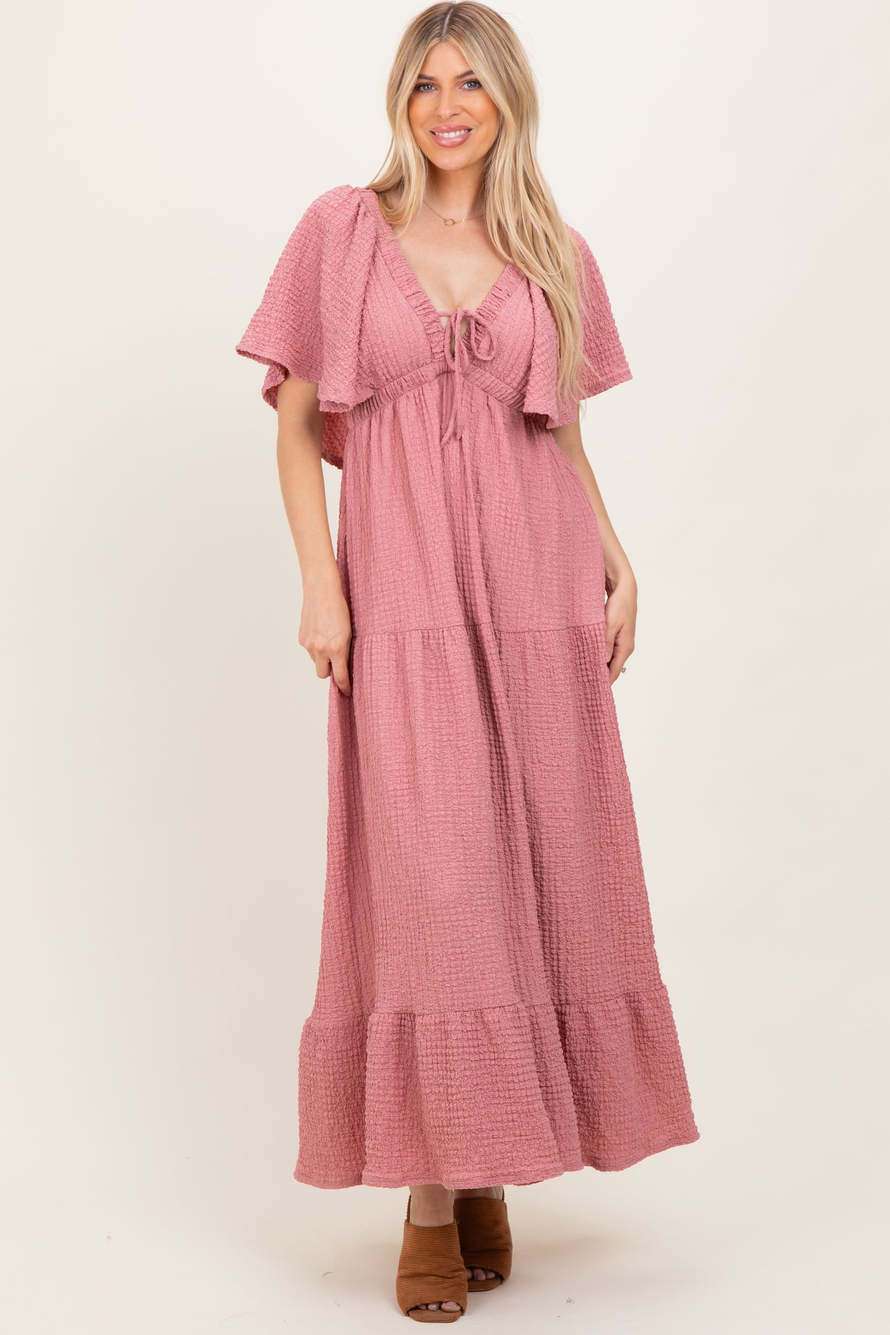 woman wearing a pink tiered maxi dress with flutter sleeves and a tie front detail