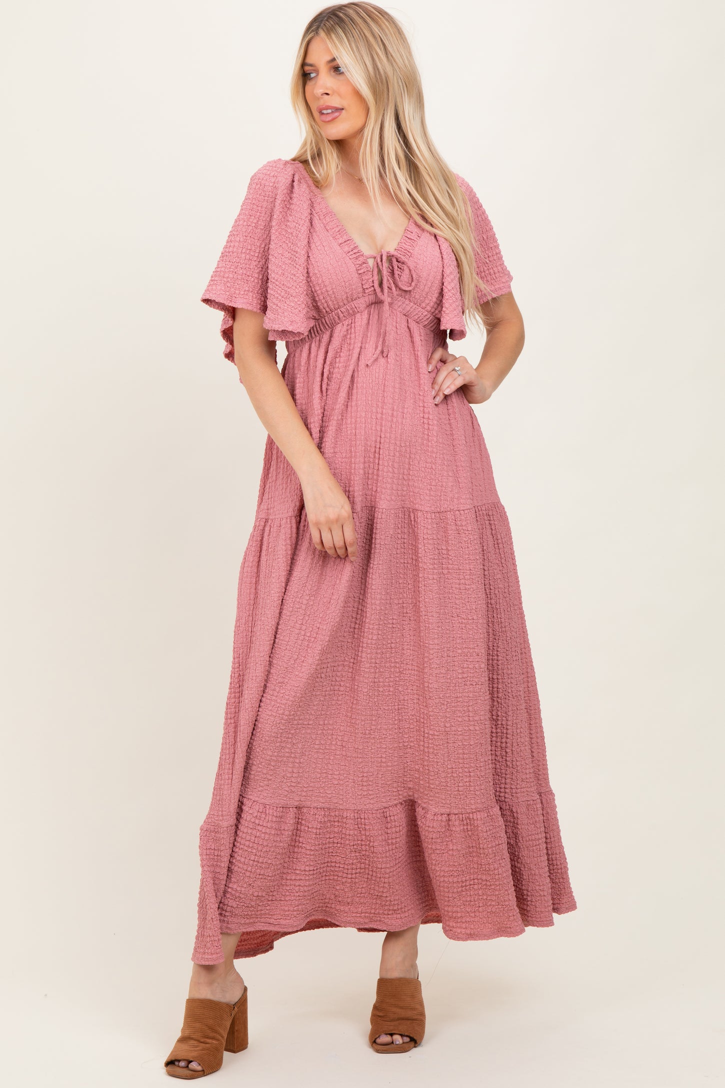 woman wearing a pink tiered maxi dress with short sleeves and a tie-front detail, standing in a relaxed pose