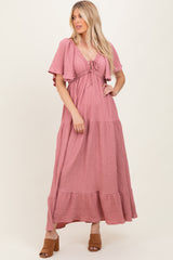 woman wearing a pink tiered maxi dress with short sleeves and a tie-front detail, standing in a relaxed pose