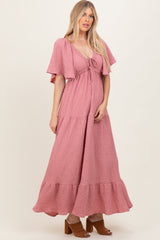woman wearing a pink wrap maxi dress with flutter sleeves and a tiered hem, standing in a casual pose